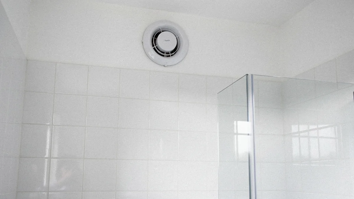 Extractor de aire instalado en la parte alta de la pared de un baño, alejado de la ducha